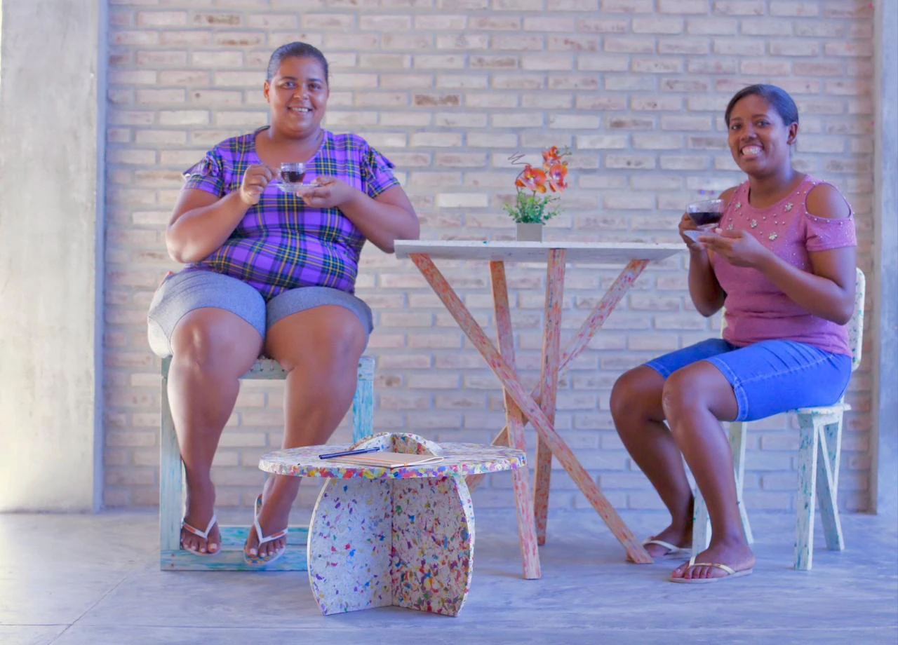 Duas mulheres sentadas junto a uma mesa e a um banco de plástico reciclado